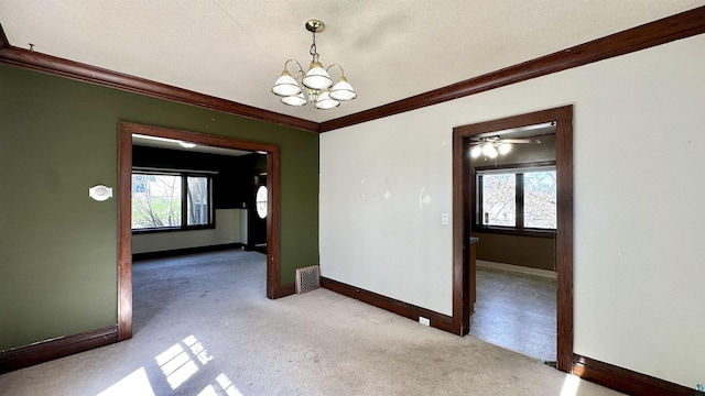spare room with crown molding, light carpet, baseboards, a chandelier, and plenty of natural light