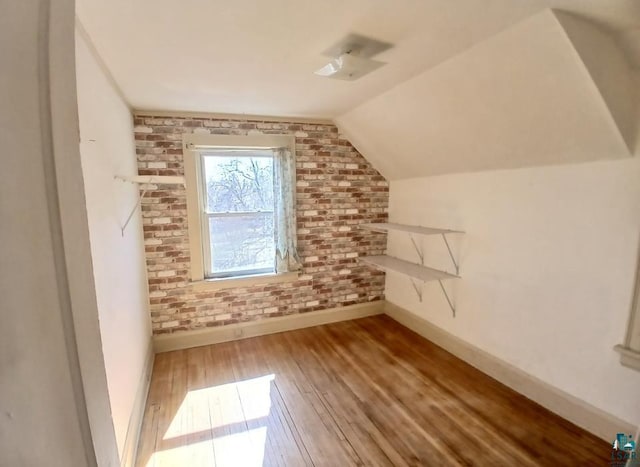 additional living space with baseboards, hardwood / wood-style flooring, vaulted ceiling, and brick wall