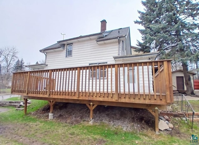 rear view of property featuring a chimney, a wooden deck, a storage shed, and an outbuilding
