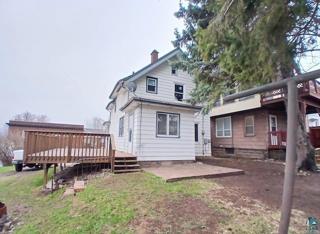 back of property with a chimney, a wooden deck, and a patio area