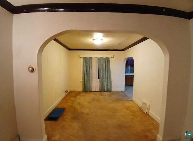 empty room featuring arched walkways, carpet, crown molding, and baseboards