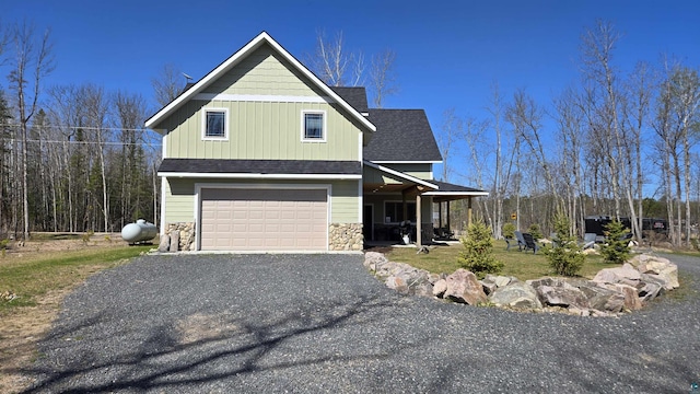 7498 Bayside Dr, Crane Lake, MN 55725 - view of front of home featuring a garage, stone siding, roof with shingles, gravel driveway, and covered porch