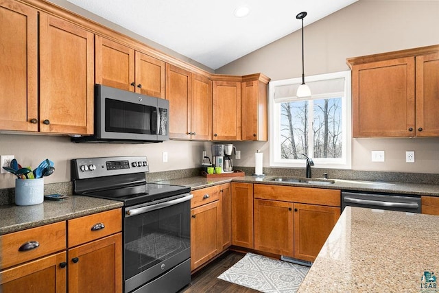kitchen featuring stainless steel appliances, lofted ceiling, a sink, brown cabinets, and decorative light fixtures