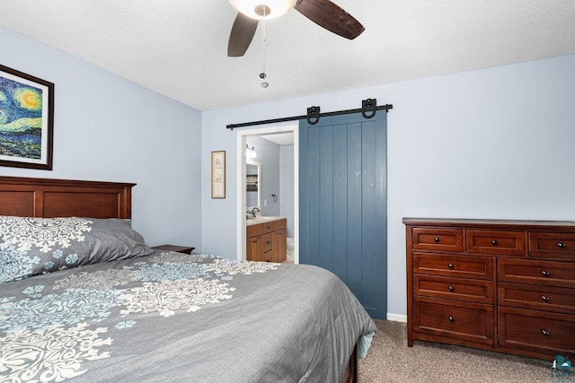 bedroom featuring light carpet, a barn door, connected bathroom, and a ceiling fan