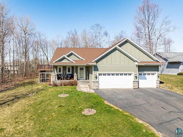view of front of home featuring board and batten siding, stone siding, asphalt driveway, an attached garage, and a front lawn
