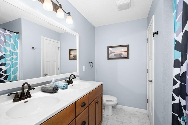 full bath with marble look tiles, toilet, double vanity, baseboards, and curtained shower