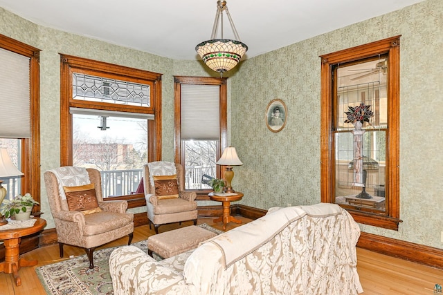 living room featuring wood-type flooring, wallpapered walls, and baseboards
