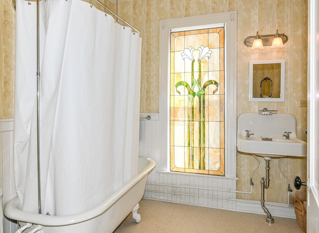full bath featuring a bathtub, a wainscoted wall, curtained shower, and a sink