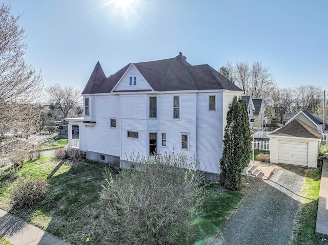 view of side of property with driveway, an outbuilding, a chimney, a detached garage, and fence