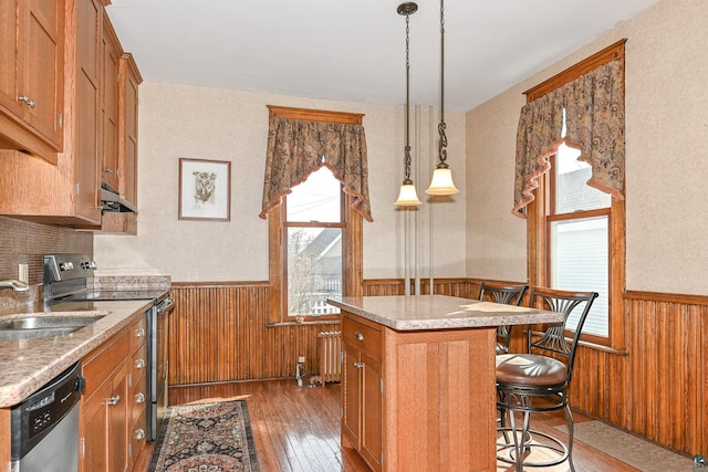 kitchen with appliances with stainless steel finishes, wainscoting, a sink, under cabinet range hood, and hardwood / wood-style flooring