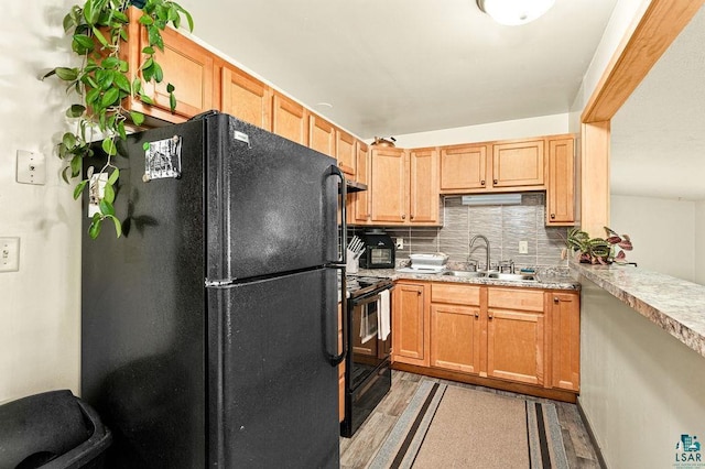 kitchen with a sink, black appliances, light wood-type flooring, and decorative backsplash