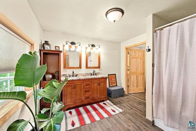 bathroom with wood finished floors, double vanity, a shower with curtain, and a textured ceiling