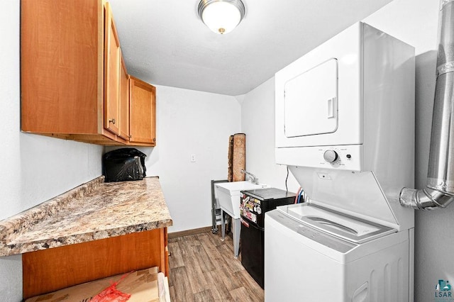 laundry area with stacked washer and clothes dryer, light wood-style flooring, baseboards, and a sink