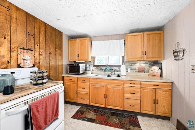 kitchen featuring white range with electric cooktop, a sink, light countertops, wood walls, and decorative backsplash