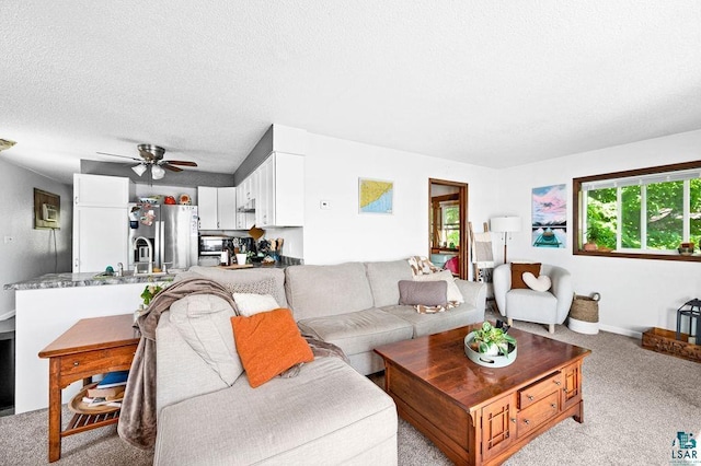 living area featuring light colored carpet, a ceiling fan, and a textured ceiling