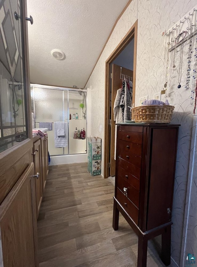 full bath featuring wood finished floors, a textured ceiling, a shower with shower door, wallpapered walls, and a textured wall