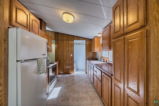 4538 Bass Lake Rd, Gilbert, MN 55741 - kitchen featuring white appliances, vaulted ceiling, a sink, brown cabinetry, and wooden walls