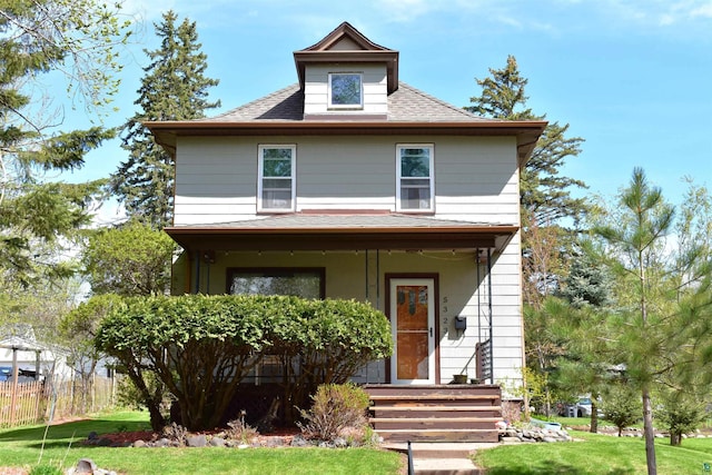 american foursquare style home featuring a porch, roof with shingles, and a front yard