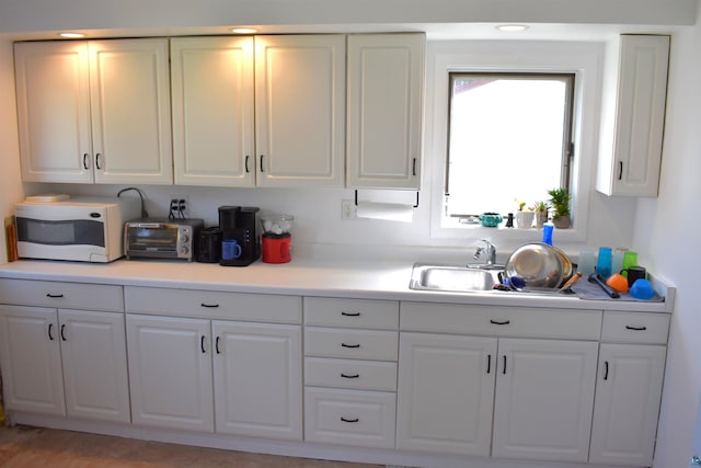 kitchen with white microwave, a sink, white cabinets, and light countertops