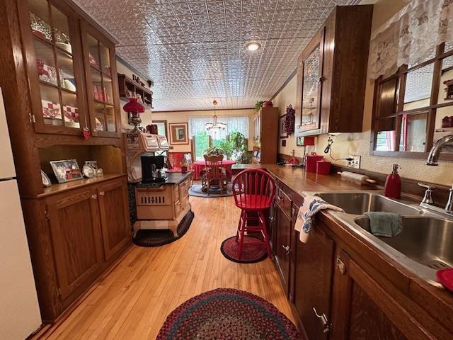1601 W 4th Ave, International Falls, MN 56649 - kitchen featuring light wood-style flooring, a sink, an ornate ceiling, glass insert cabinets, and pendant lighting