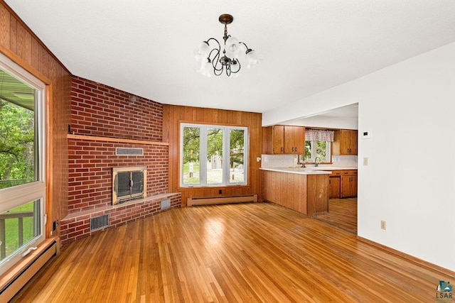 4724 E Ayers Rd, Saginaw, MN 55779 - unfurnished living room with a baseboard heating unit, baseboard heating, light wood finished floors, a chandelier, and a brick fireplace