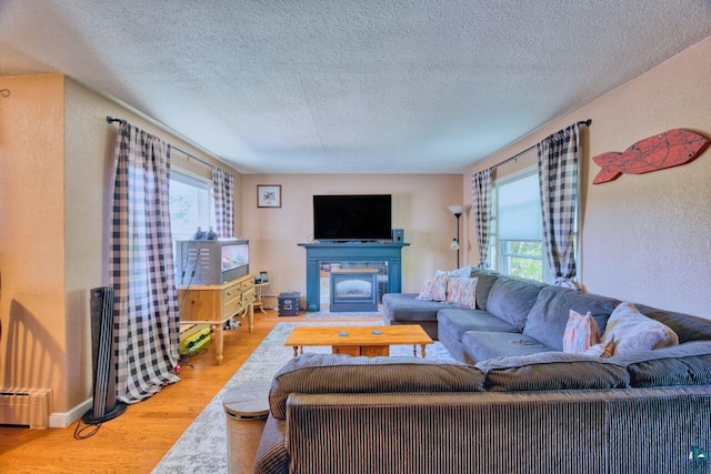 305 W Central Ave, Aurora, MN 55705 - living area featuring wood finished floors, a textured ceiling, a glass covered fireplace, a textured wall, and baseboard heating