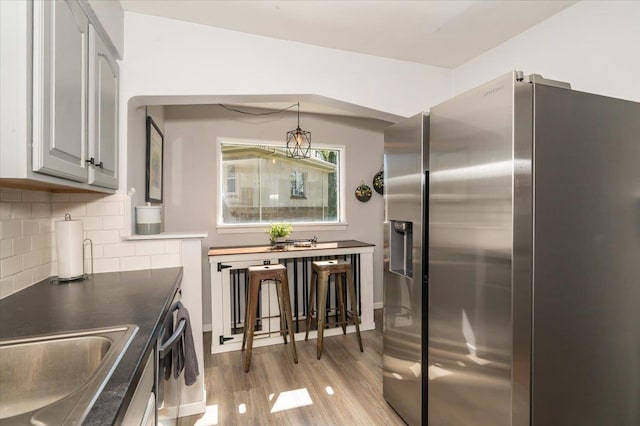 5521 Huntington St, Duluth, MN 55807 - kitchen with stainless steel refrigerator with ice dispenser, backsplash, light wood finished floors, dark countertops, and decorative light fixtures