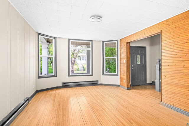 2626 W 5th St, Duluth, MN 55806 - empty room with a baseboard heating unit, light wood-type flooring, and wooden walls