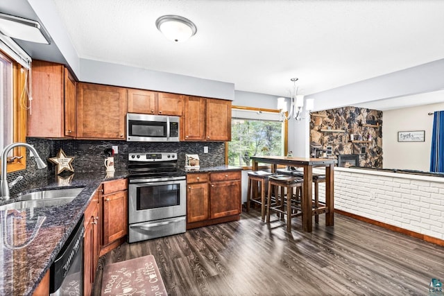 4750 Morris Thomas Rd, Hermantown, MN 55811 - kitchen featuring appliances with stainless steel finishes, brown cabinets, dark wood-style floors, decorative backsplash, and a chandelier