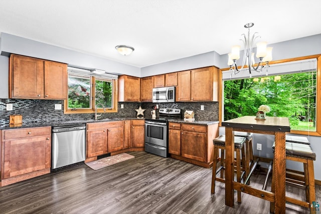 4750 Morris Thomas Rd, Hermantown, MN 55811 - kitchen featuring appliances with stainless steel finishes, a chandelier, brown cabinets, dark wood-style flooring, and decorative backsplash