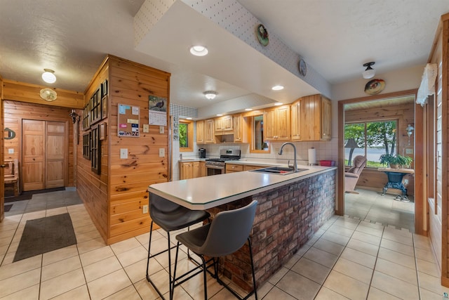 4930 Mini Power Rd, Duluth, MN 55803 - kitchen with gas stove, wood walls, light countertops, light tile patterned floors, and a peninsula