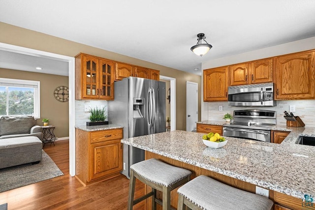 1207 Jean Marie St, Cloquet, MN 55720 - kitchen featuring appliances with stainless steel finishes, glass insert cabinets, brown cabinetry, light stone counters, and tasteful backsplash
