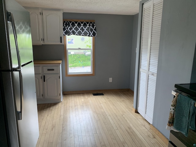 3118 Exeter St, Duluth, MN 55806 - kitchen with freestanding refrigerator, light wood finished floors, stove, a textured ceiling, and white cabinets