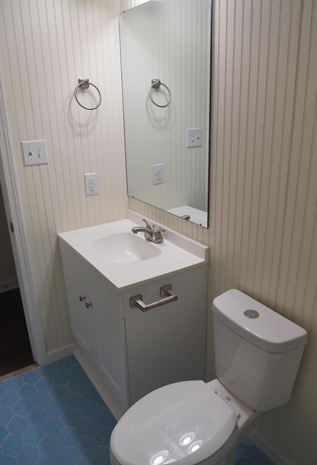 bathroom with wooden walls, tile patterned flooring, vanity, and toilet