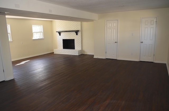 unfurnished living room with dark hardwood / wood-style flooring, a textured ceiling, and a brick fireplace