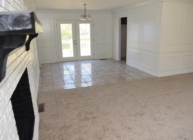 unfurnished living room featuring french doors, a brick fireplace, ornamental molding, light colored carpet, and a chandelier