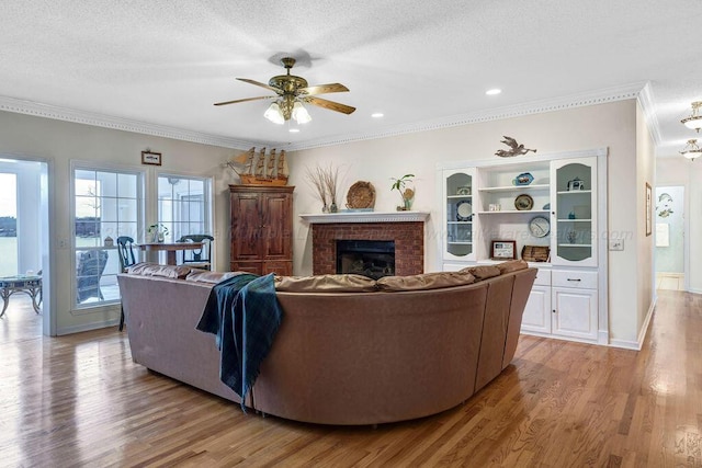 living room with a brick fireplace, crown molding, and light wood-style flooring