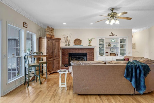 living area featuring light wood-type flooring, a brick fireplace, a ceiling fan, and crown molding