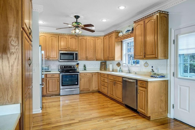 kitchen with light wood finished floors, stainless steel appliances, light countertops, a ceiling fan, and a sink