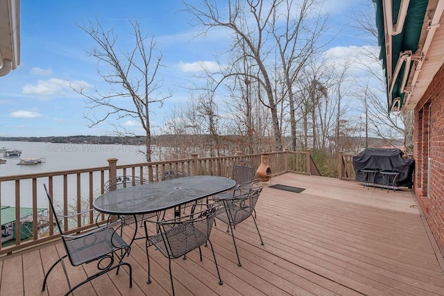 deck with outdoor dining space, area for grilling, and a water view