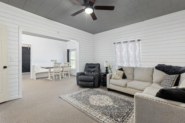 carpeted living room with ceiling fan and wooden walls