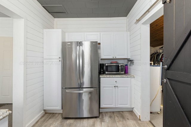 kitchen featuring wood walls, white cabinetry, light stone counters, stainless steel appliances, and light wood-type flooring