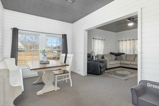 dining area featuring ceiling fan, wooden walls, a healthy amount of sunlight, and carpet flooring