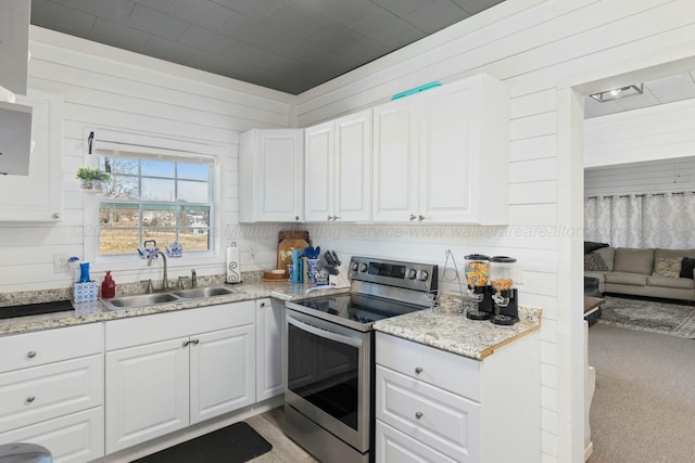 kitchen with wood walls, white cabinetry, sink, stainless steel range with electric cooktop, and light stone counters