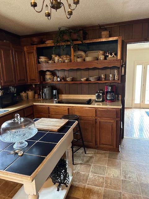 kitchen featuring an inviting chandelier, black electric stovetop, a textured ceiling, and wood walls