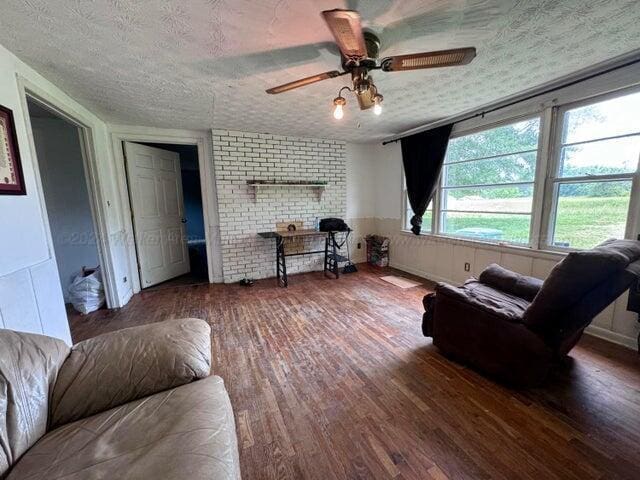 living room featuring ceiling fan, hardwood / wood-style floors, brick wall, and a textured ceiling