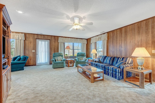 carpeted living room with ceiling fan, ornamental molding, wooden walls, and a textured ceiling