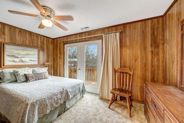 carpeted bedroom with ornamental molding, access to exterior, a textured ceiling, and wood walls