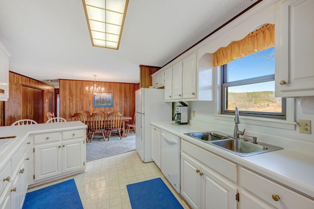 kitchen featuring sink, wood walls, hanging light fixtures, white appliances, and white cabinets