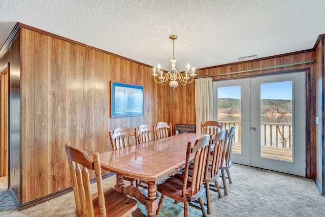 dining room with light colored carpet, wood walls, a textured ceiling, and french doors